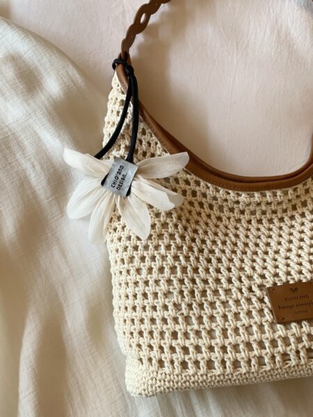 Beige woven crochet tote bag with brown trim and flower charm