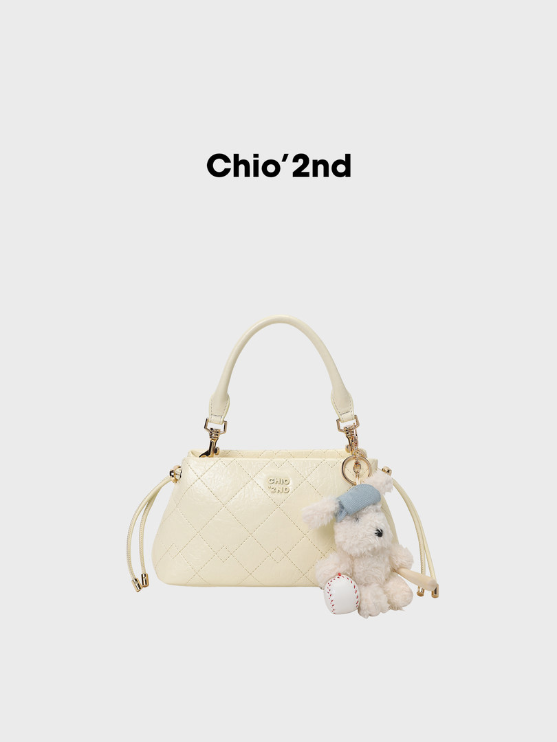 Cream quilted handbag with teddy bear charm on a plain background