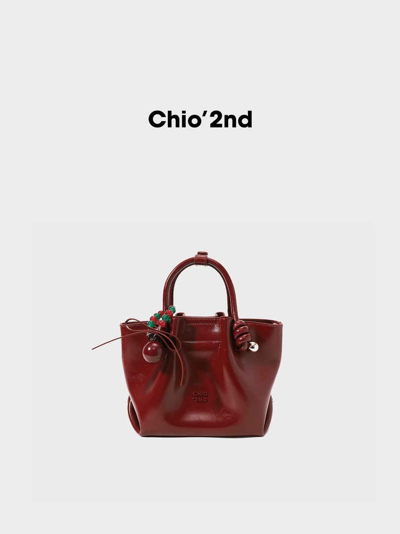 Red glossy handbag with bead charm and top handles on a white background