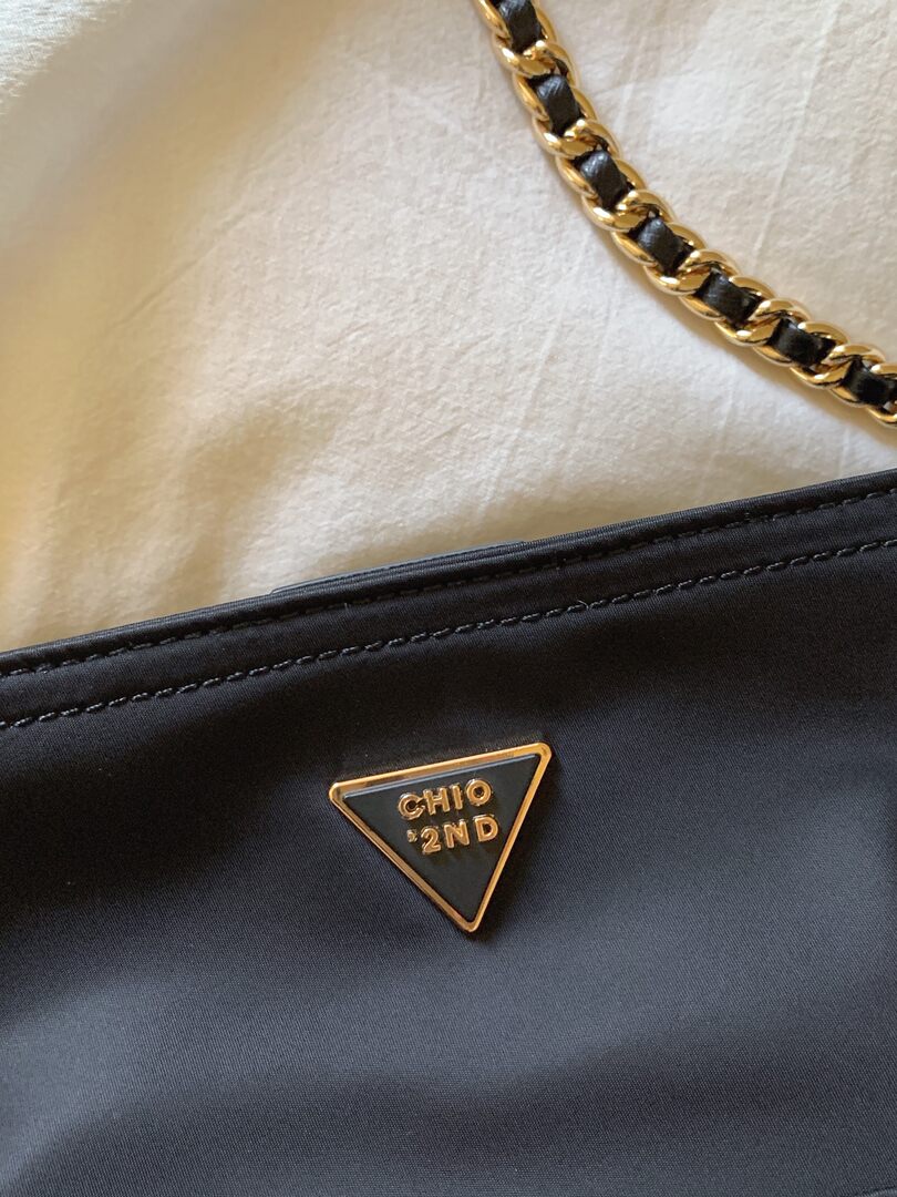 Close-up of a black handbag with a gold chain and logo emblem