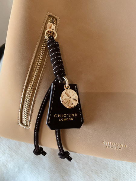 Beige leather handbag with gold zipper and black hanging charm