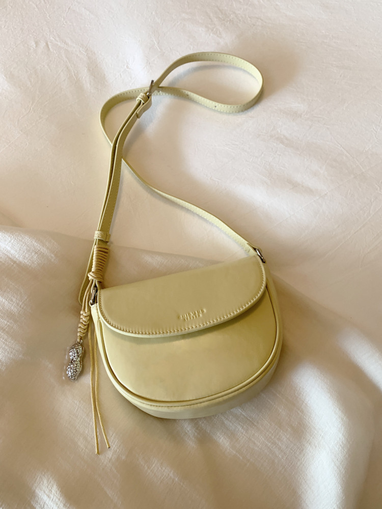 Light yellow crossbody handbag with a flap closure on a soft fabric background