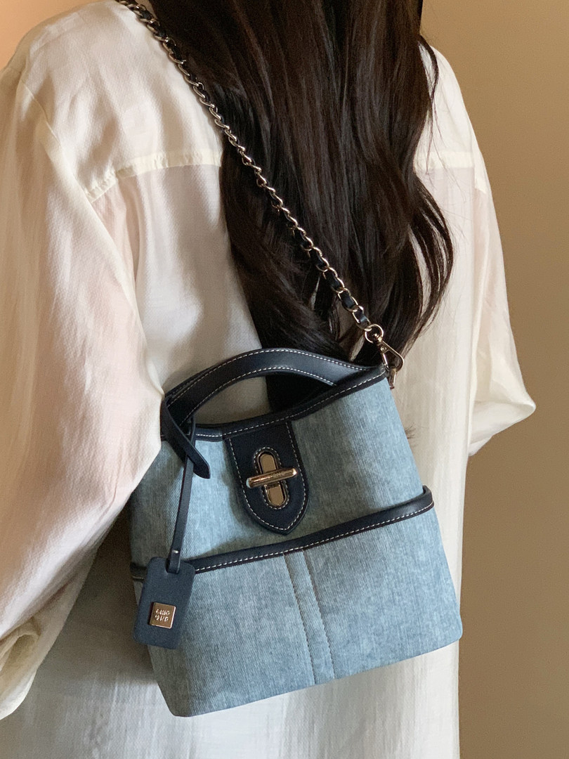 Blue denim shoulder bag with black trim and chain strap worn on a model