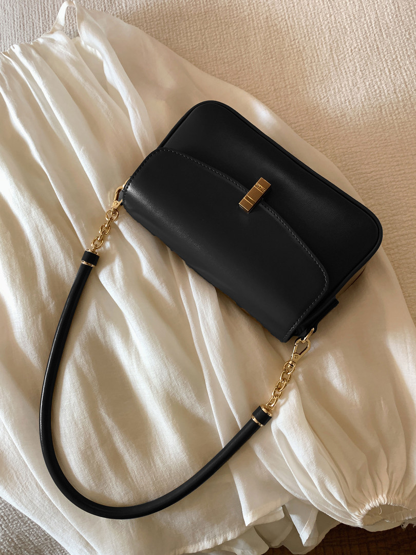 Black leather shoulder handbag with gold hardware on a cream fabric background