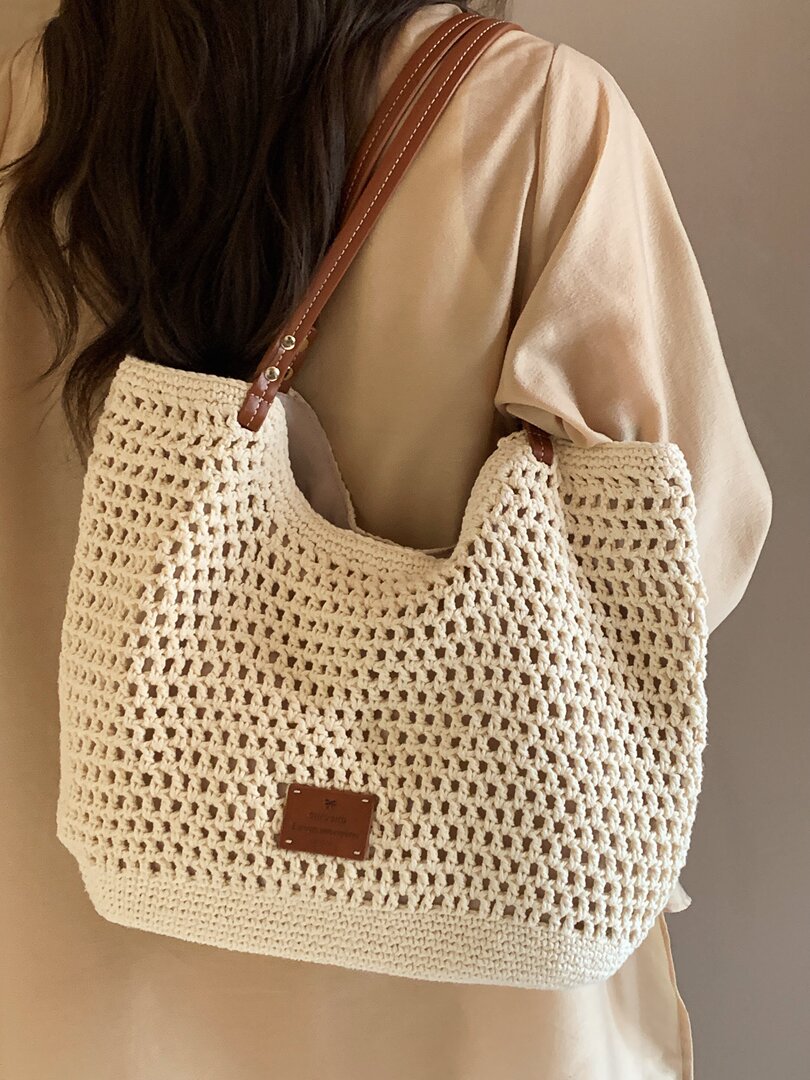 Crocheted cream tote bag with brown leather straps worn over the shoulder