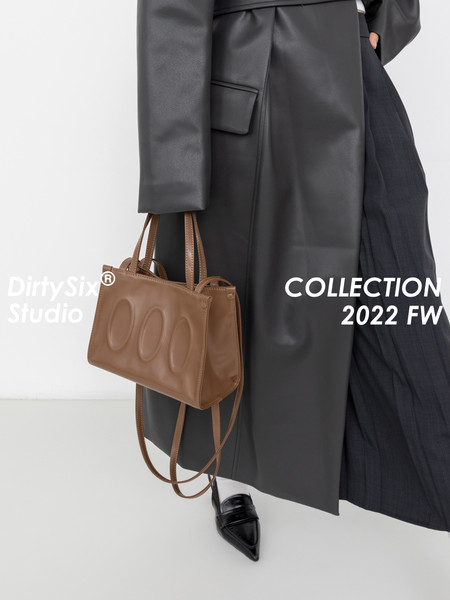 Brown leather handbag carried with a black coat and skirt on a model