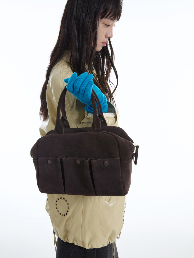 Dark brown handbag held by a model on a white background
