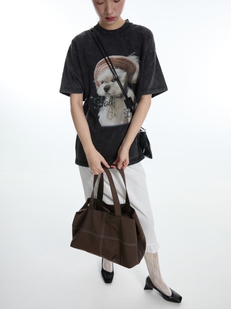 Model wearing a black graphic oversized T-shirt with a brown tote bag