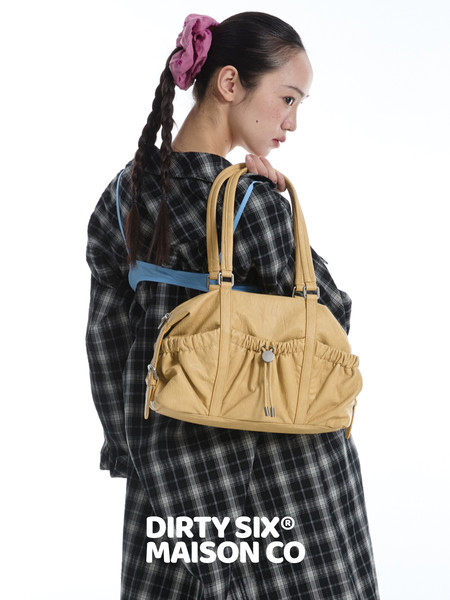 Model wearing a tan shoulder handbag with a black plaid outfit on a white background