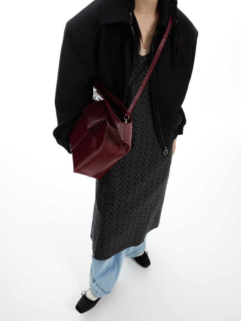 Model wearing a black jacket, patterned dress, jeans, and burgundy shoulder bag
