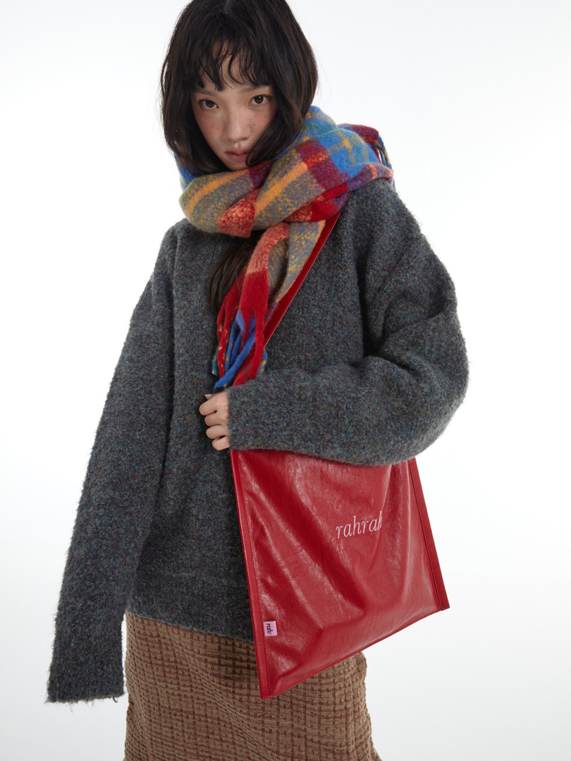 Model wearing a chunky dark sweater with a colorful plaid scarf and red tote bag