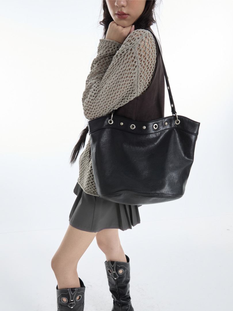 Black leather tote bag worn by a model with a casual outfit