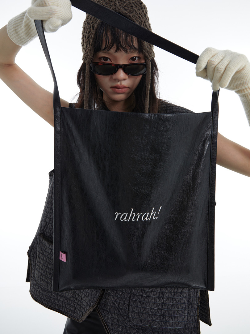 Black leather tote bag held by a model against a white background