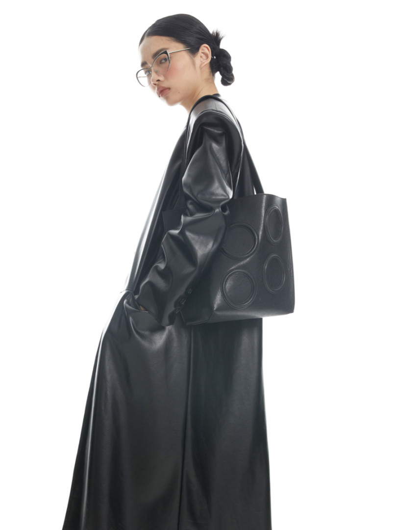 Model wearing a black leather coat with a black tote bag