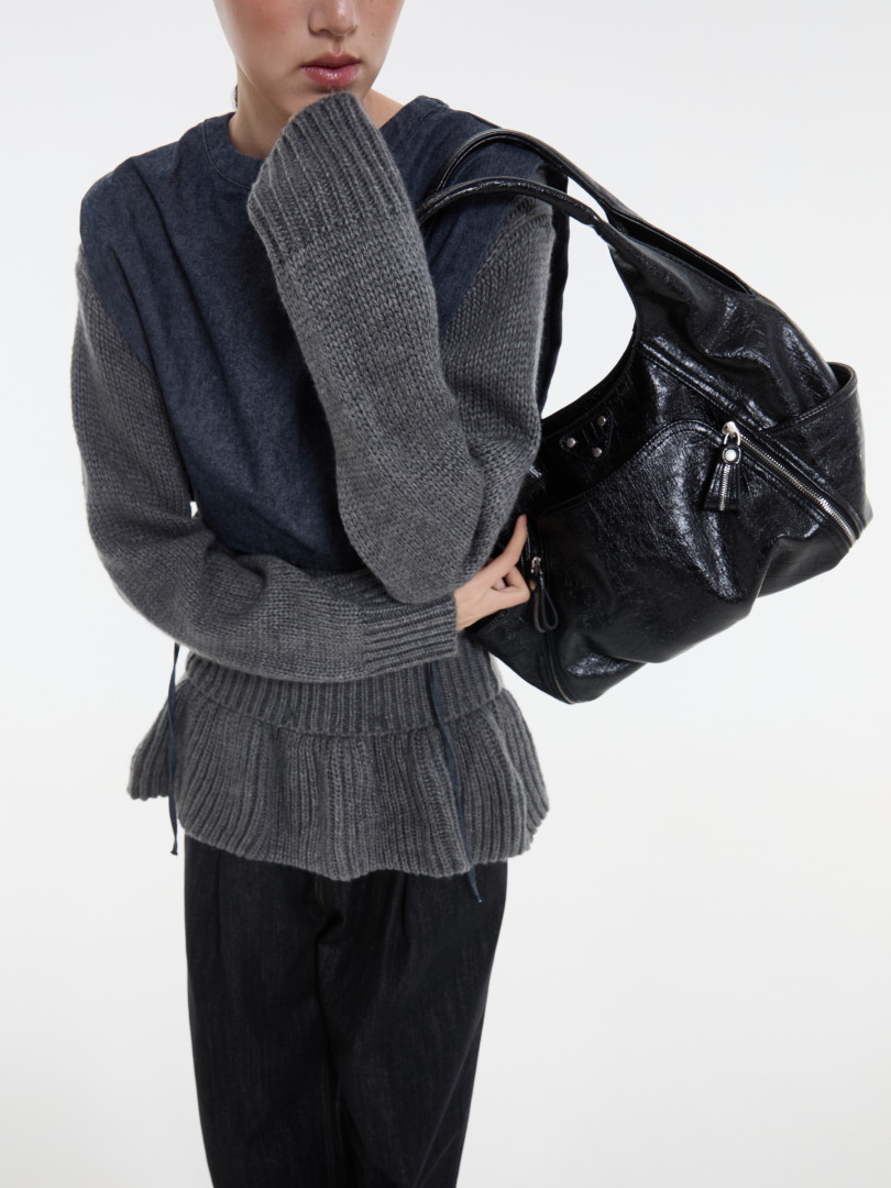 Model wearing a gray knit sweater and holding a black glossy shoulder bag