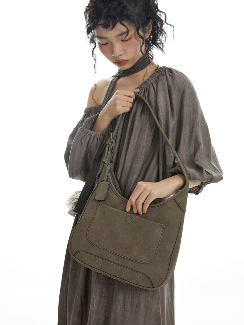 Model wearing a taupe off-shoulder dress and holding an olive shoulder bag