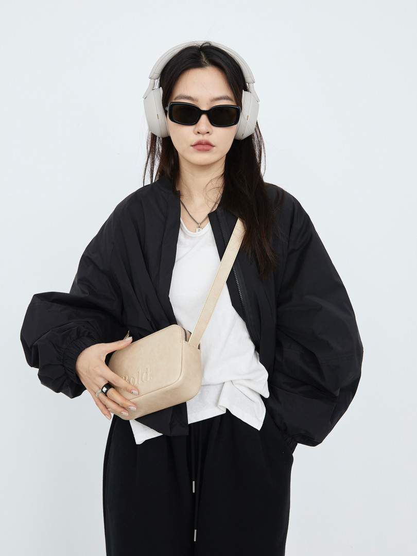 Model wearing a black oversized jacket with a beige crossbody bag