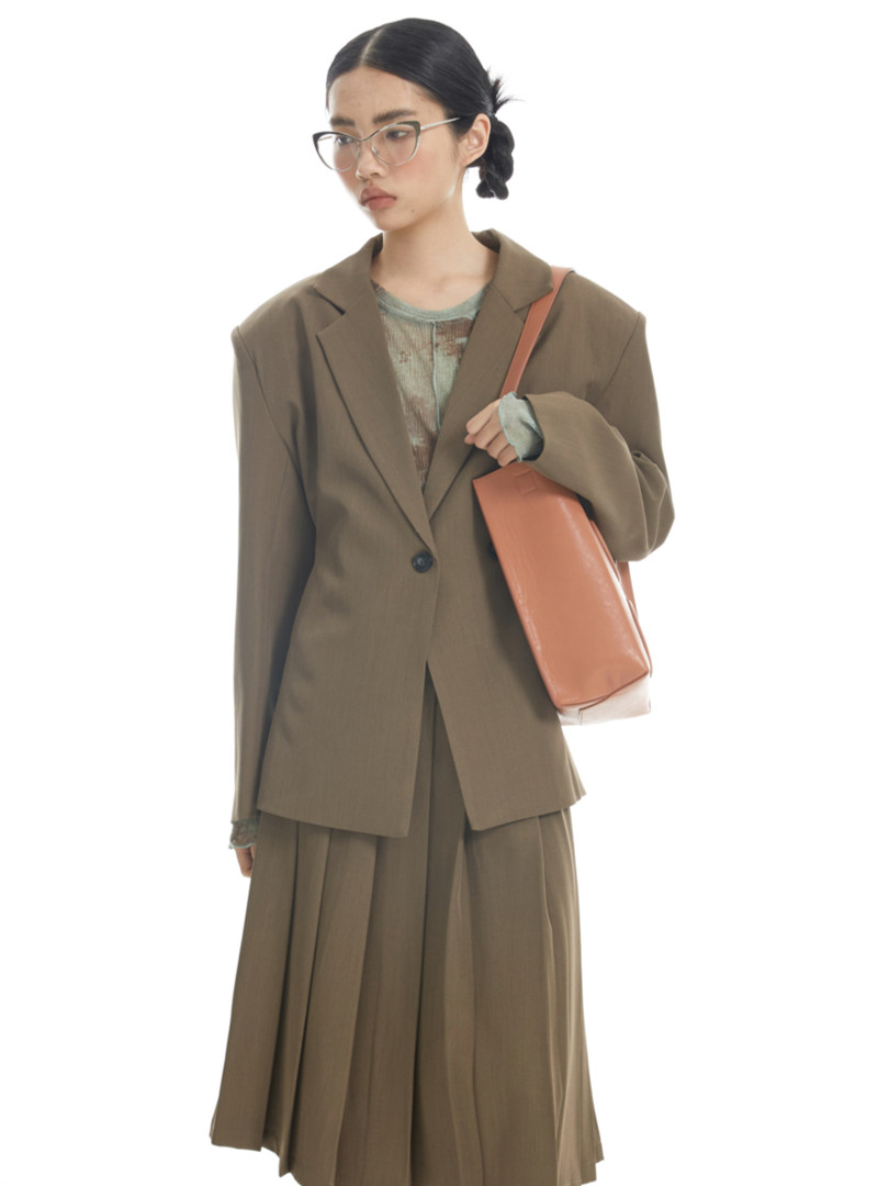 Woman modeling an olive-brown blazer and pleated skirt set with a tote bag