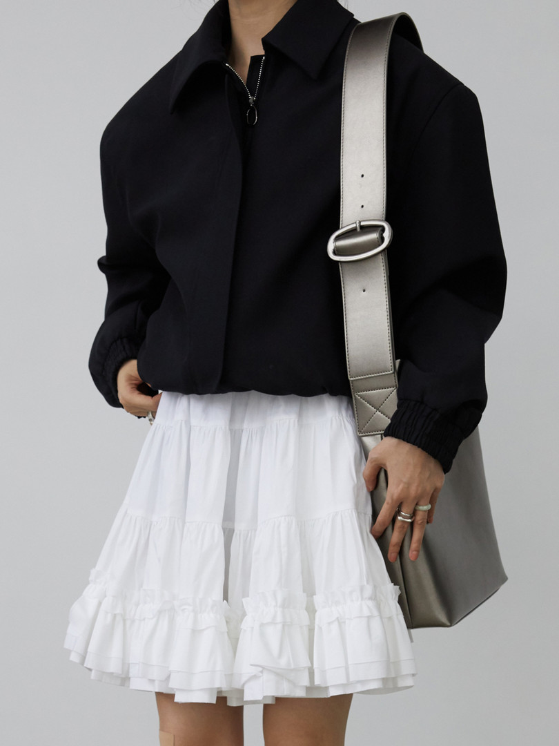 Model wearing a black cropped top with a white tiered skirt and shoulder bag