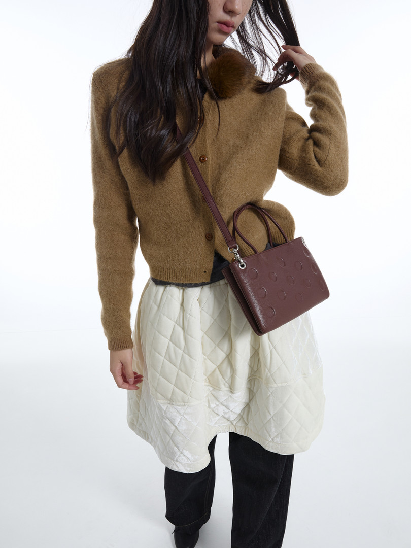 Model wearing a brown fuzzy cardigan with a burgundy crossbody bag and quilted skirt