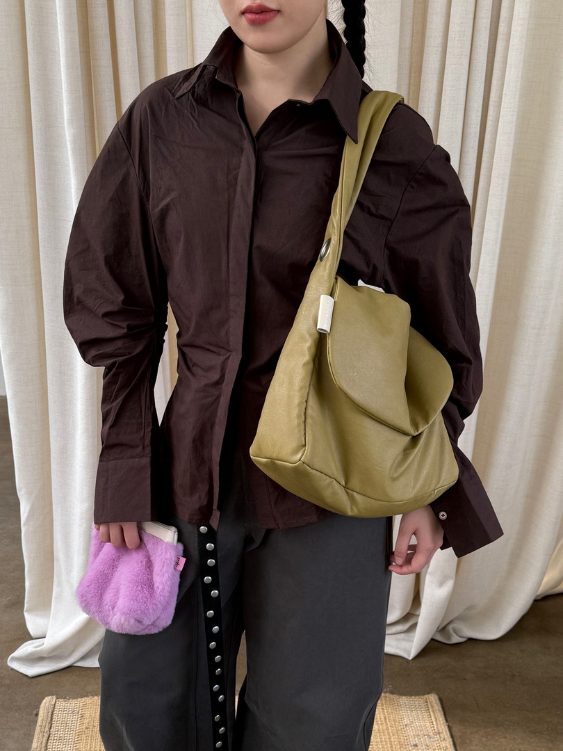 Model wearing a dark brown oversized shirt with an olive shoulder bag and gray pants