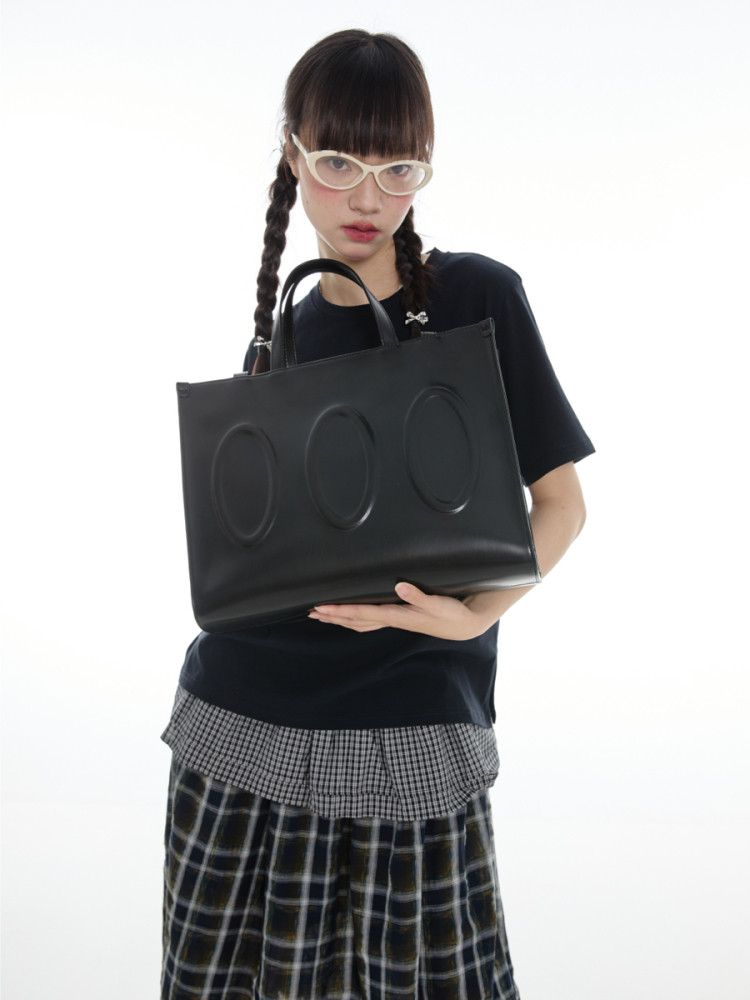 Black tote bag held by a model on a white background