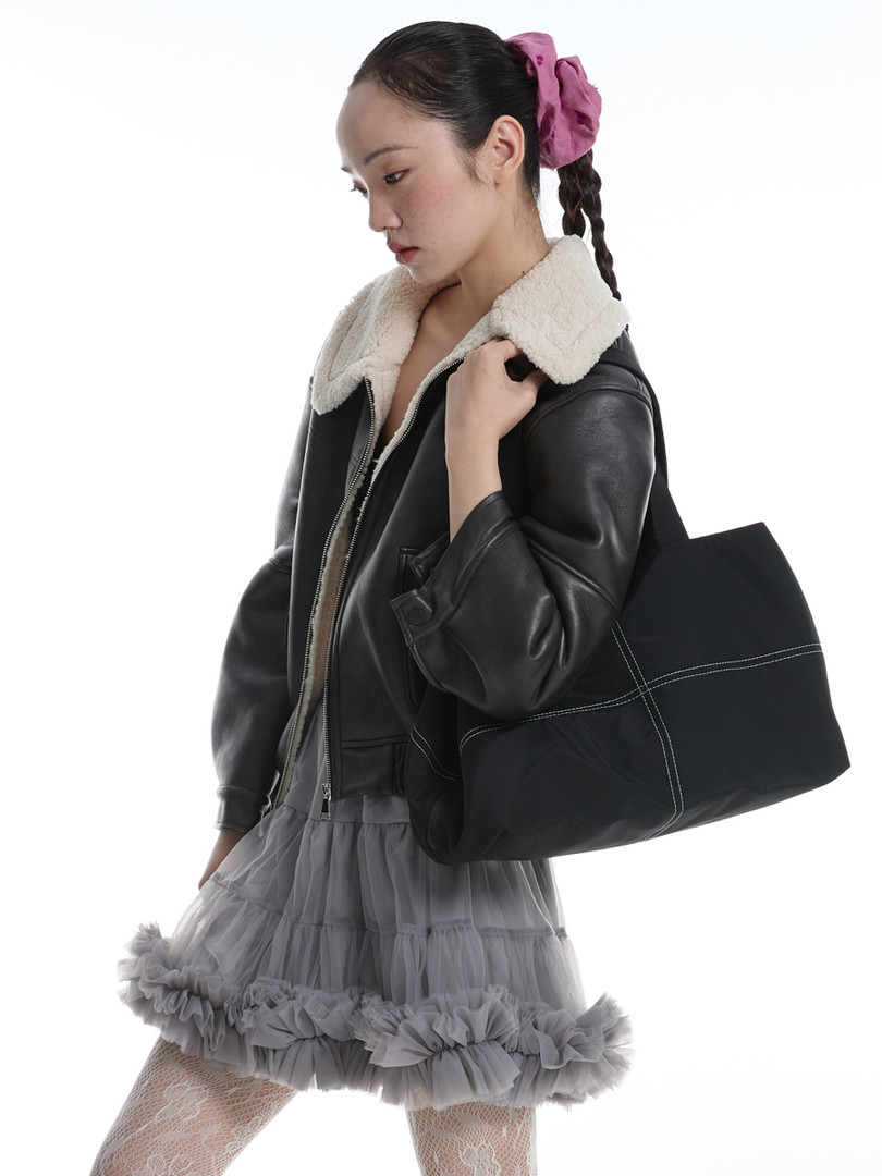 Fashion model wearing a black shearling-collar leather jacket with a gray ruffled skirt and black tote bag