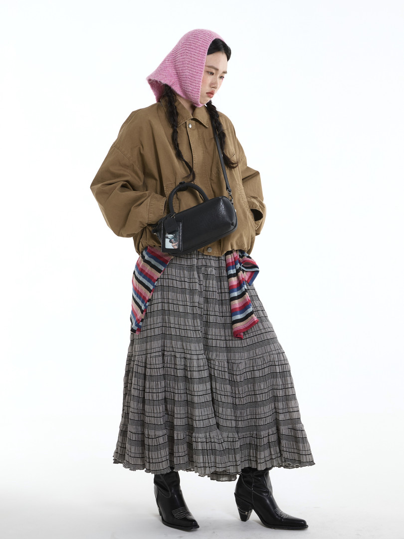 Fashion model wearing a brown jacket, gray skirt, black boots, and a black handbag