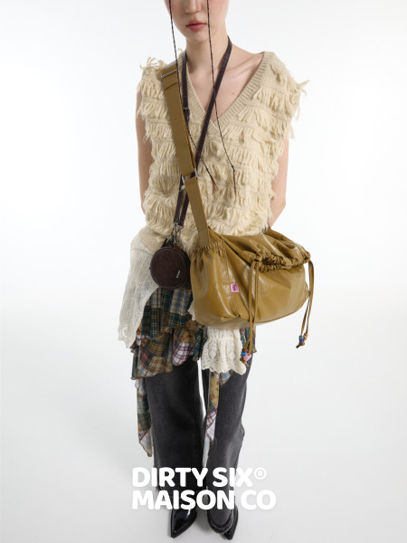 Fashion model wearing a textured cream vest with a tan crossbody bag and layered casual outfit
