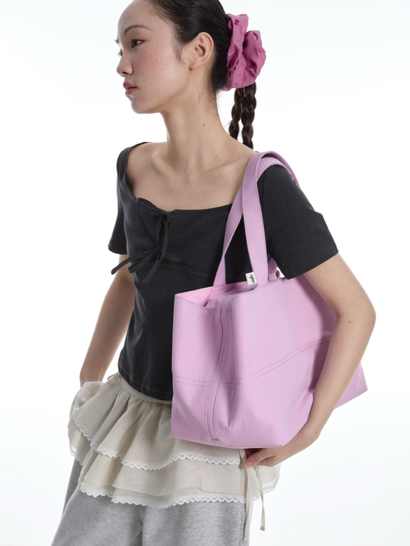 Model wearing a black top and carrying a pink tote bag