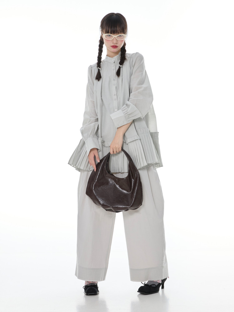 Model wearing a light gray loose outfit and holding a dark brown handbag