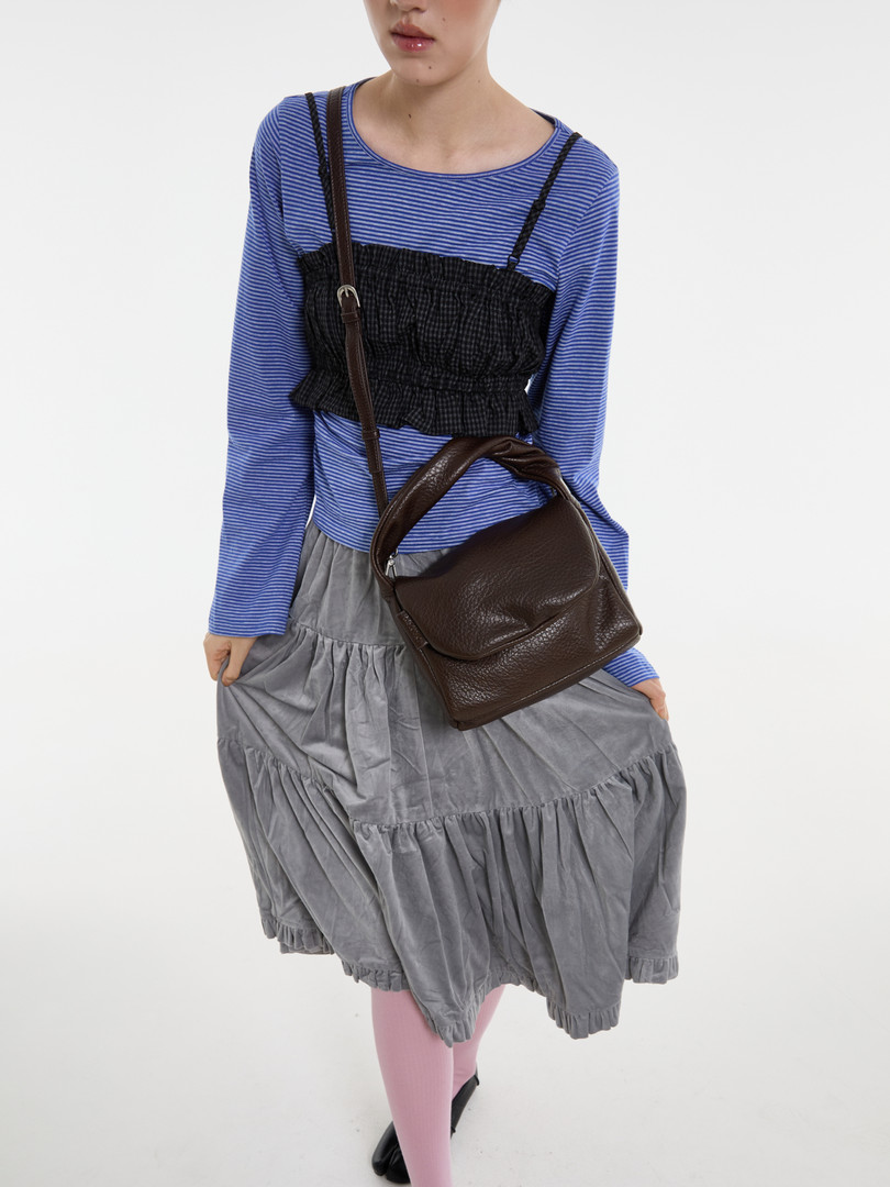 Model wearing layered striped top, black camisole dress, gray skirt, and brown shoulder bag