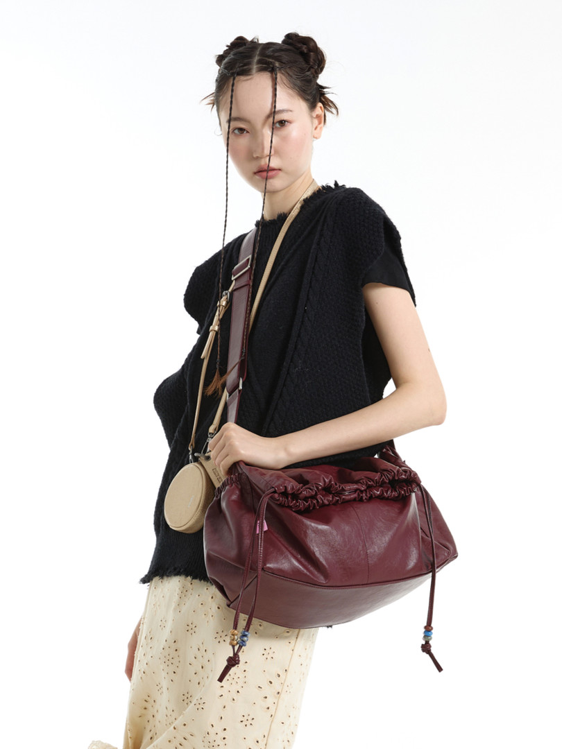 Model wearing a black outfit with a burgundy leather shoulder bag