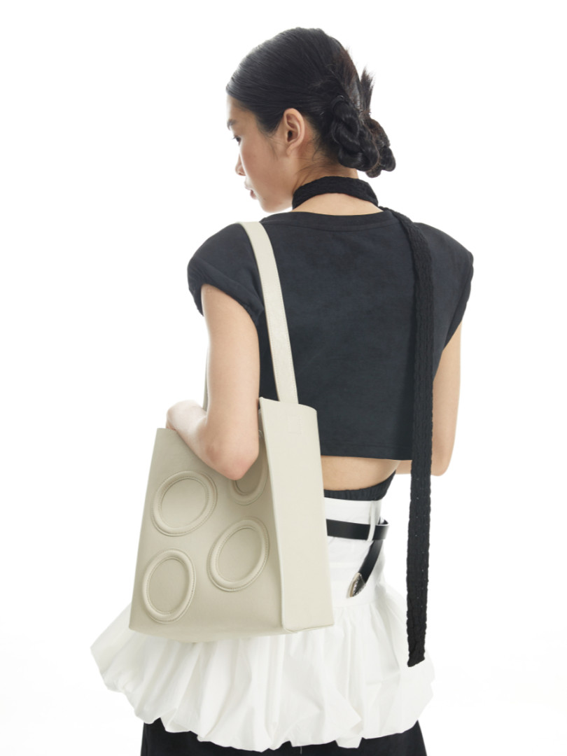 Woman wearing a black crop top and white skirt with a beige tote bag on a white background