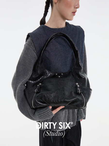 Black leather shoulder bag worn by a model with a gray knit sweater