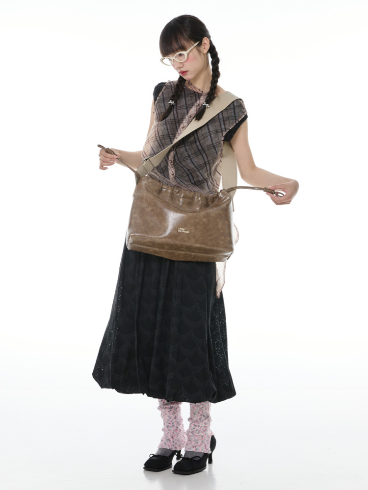 Model wearing a plaid top, long black skirt, and brown shoulder bag on a white background