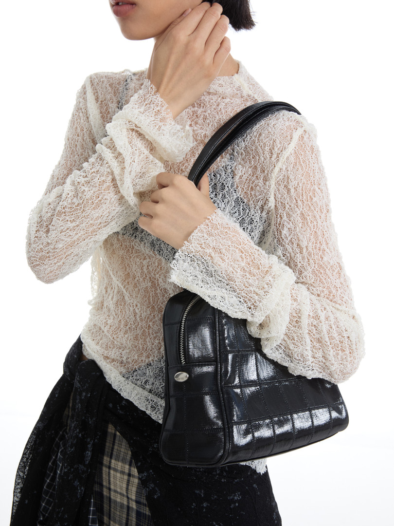 Model wearing a sheer white lace top and carrying a black quilted handbag