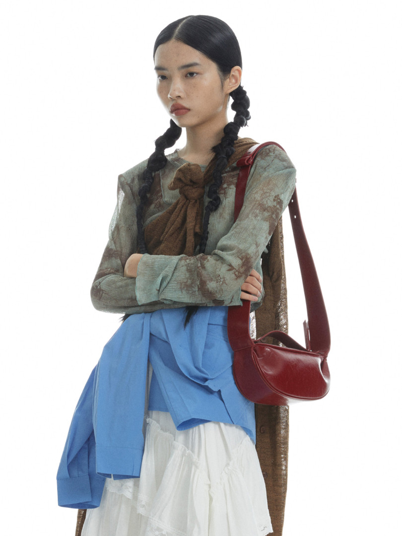 Fashion model wearing layered outfit with a red shoulder bag on a white background