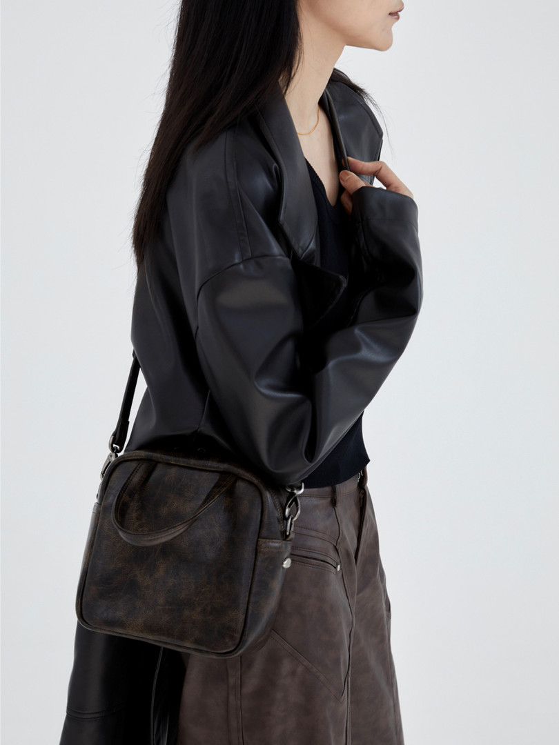 Model wearing a black leather jacket and dark crossbody bag