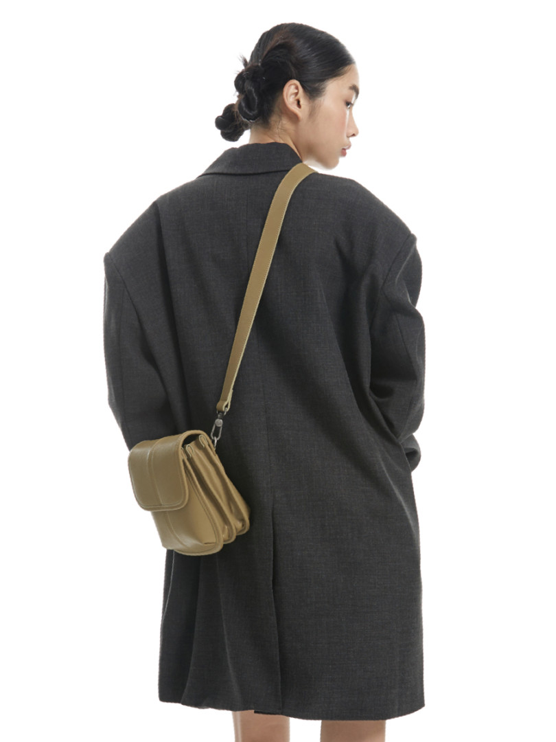 Model wearing a dark oversized coat with a tan crossbody bag