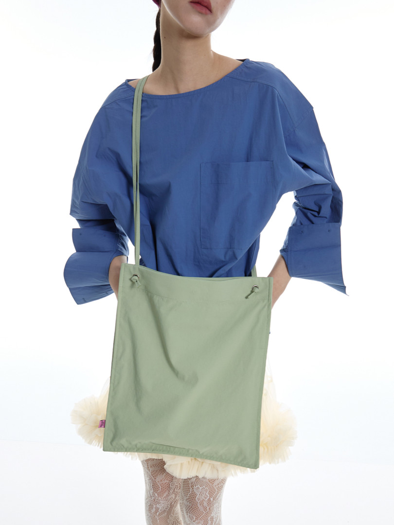 Model wearing a blue oversized top with a mint green crossbody bag