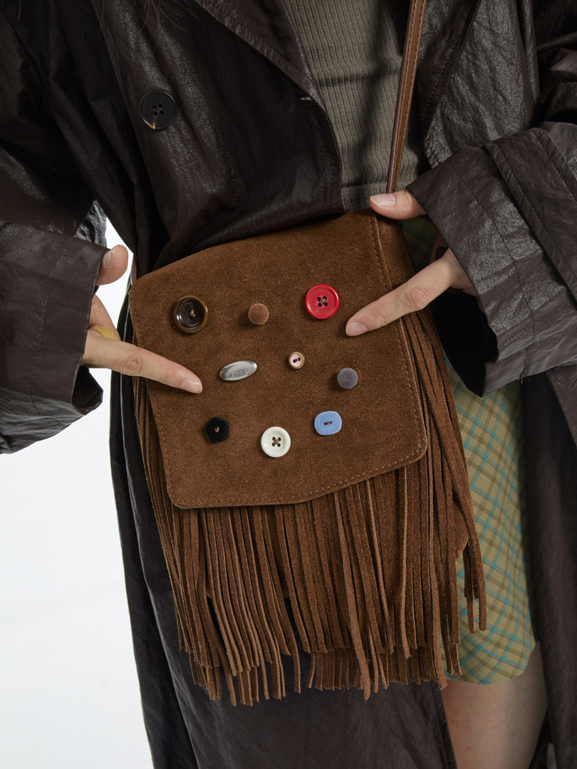 Brown suede fringe crossbody bag with decorative buttons worn by a model