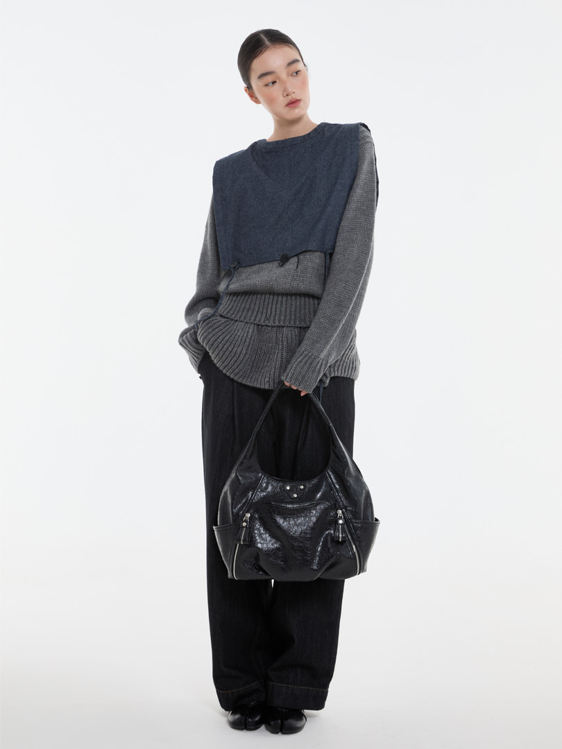Model wearing a layered knit outfit and holding a black leather shoulder bag