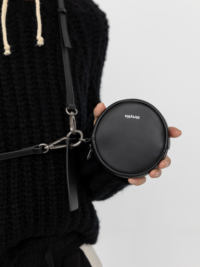 Black round crossbody bag with strap held in hand