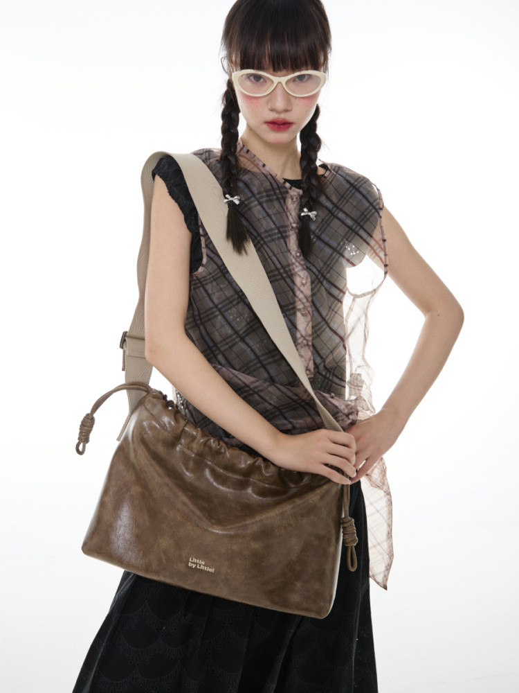 Model wearing a brown leather crossbody bag with a plaid top and glasses