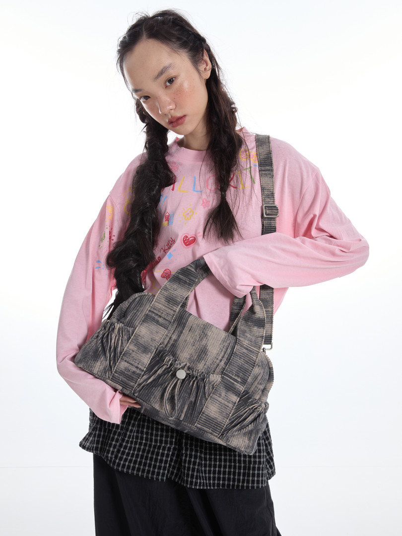 Model wearing a pink graphic sweatshirt and holding a gray shoulder bag
