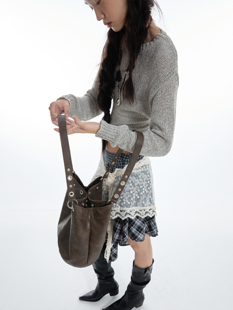 Fashion model wearing a gray knit sweater with a brown leather shoulder bag, plaid skirt, and black boots