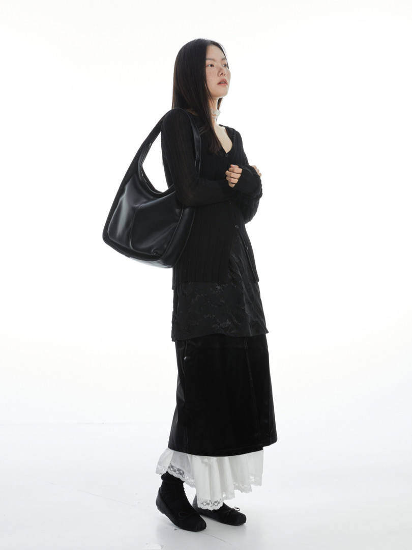 Model wearing a black layered outfit with a large black shoulder bag