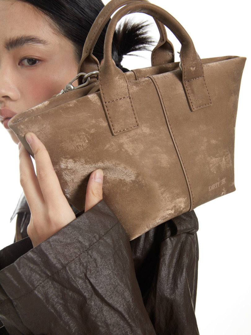 Brown leather handbag held by a woman on a white background