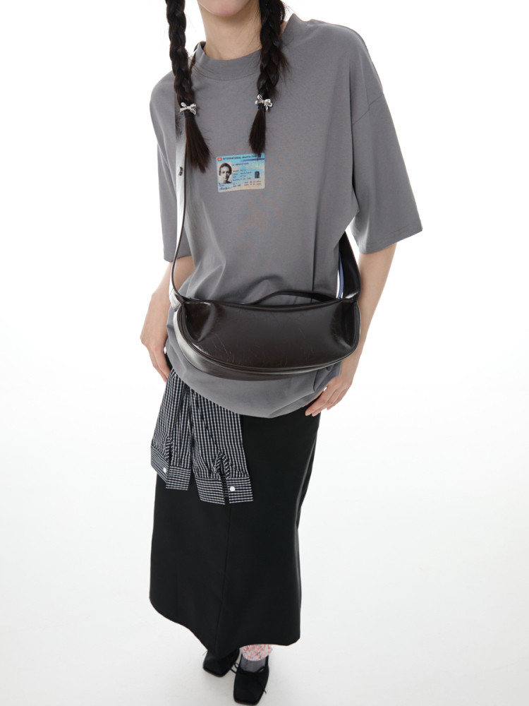 Model wearing a gray oversized T-shirt with a black crossbody bag and layered skirt.